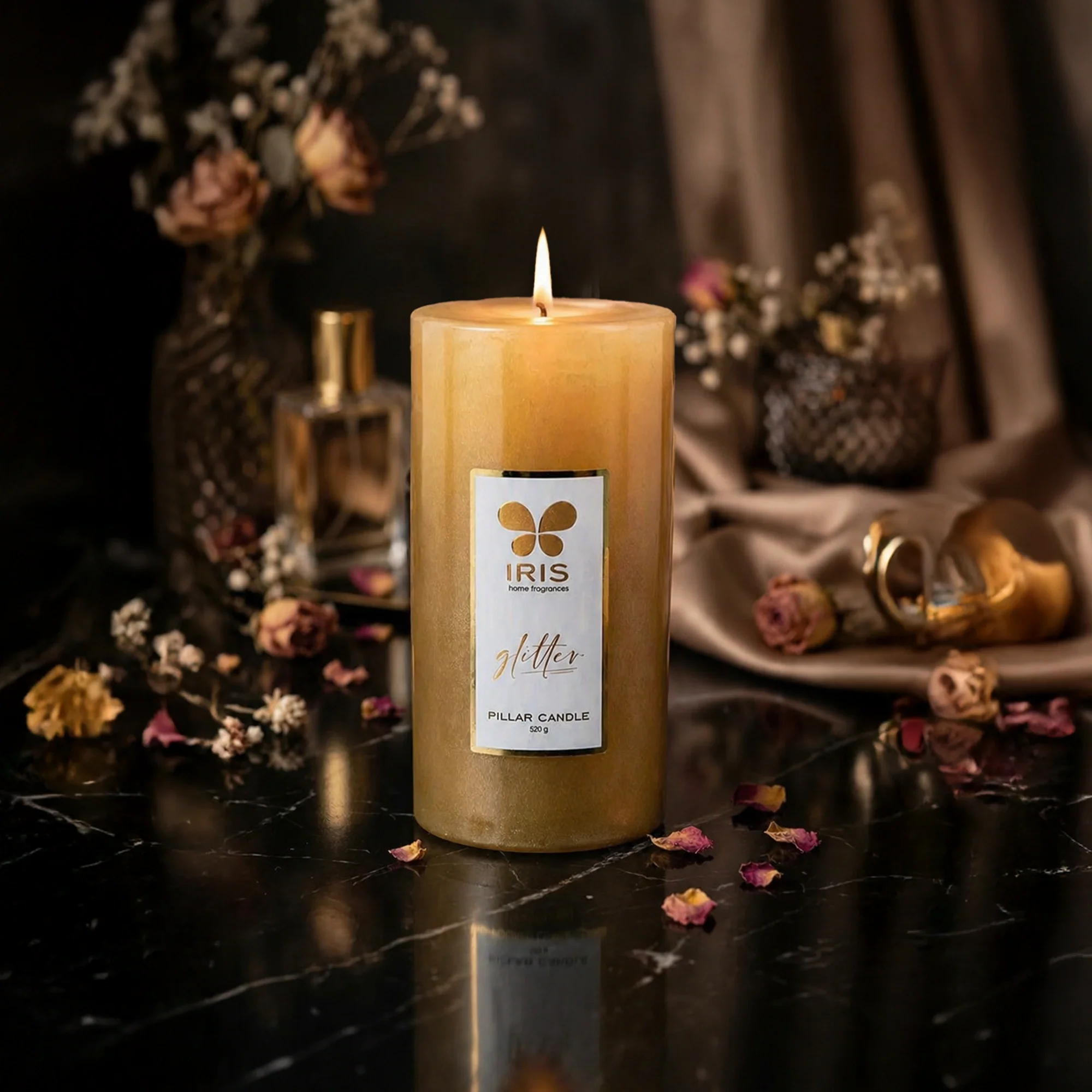 Glowing gold pillar candle with dried roses on dark marble